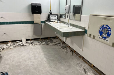 Womens restroom with old flooring and bottom row of tile demolished